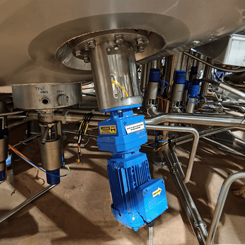Base entry agitator mounted to the conical base of a stainless steel tank. The motor is blue. The mixer is mounted via bolts to an opening.